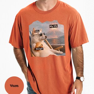 May include: Orange t-shirt with a graphic of a dog wearing sunglasses, holding a burger, and relaxing on a beach chair. The image includes the text "Me", "Burger", and "My life".