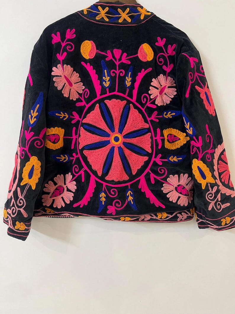 以下が含まれることがあります： ピンク、オレンジ、青色の鮮やかな花柄刺繍が施された黒いジャケット。背中には丸い花柄のデザイン、袖と襟には詳細な模様があります。刺繍は、暗い生地にカラフルなコントラストを加えています。