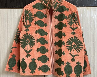 May include: A peach-colored jacket featuring dark green embroidered floral and pomegranate motifs. The garment has a high collar, long sleeves, and an open front design that reveals a red and white vertically striped lining on the interior.