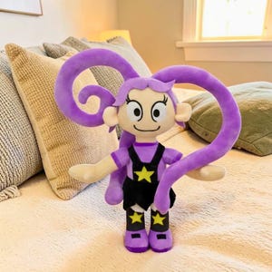 Pode incluir: Boneca de pelúcia com design de desenho animado. A boneca tem um esquema de cores roxo, incluindo cabelo longo e encaracolado e botas. Ela usa uma camisa roxa, macacão preto com uma estrela amarela e tem um rosto sorridente.