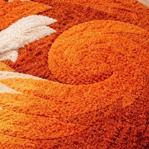 May include: A round, orange fox-shaped rug with a fluffy texture. The rug features a fox's head, ears, and curled tail in shades of orange and cream. This decorative rug is designed for a child's room or nursery.