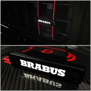 Könnte beinhalten: Nahaufnahme eines schwarzen Kühlergrills mit dem Wort "BRABUS" in weißer Schrift. Der Kühlergrill hat rote Akzentlinien. Das zweite Bild zeigt ein schwarzes Emblem mit dem Wort "BRABUS" in weißer Schrift, mit einem Kohlefaserhintergrund.