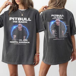 May include: Dark gray t-shirt featuring the text "PITBULL I'M BACK" above an image of Pitbull and Lil Jon. The shirt also lists "NORTH AMERICA" and "OPENING DJ SET BY DJ LAX". The back of the shirt has a tour schedule.