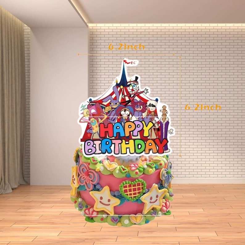 Op de afbeelding: Een versierde verjaardagstaart met een kleurrijke circus-thema topper met de tekst "Happy Birthday". De taart is roze met gele en groene frosting en stervormige decoraties. De topper is 15,7 cm hoog.