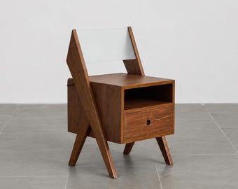 Puede incluir: Una silla de madera con una base en forma de caja que incluye un compartimento de almacenamiento abierto y un cajón con un tirador circular. La silla tiene patas inclinadas y un respaldo blanco plano que se extiende hacia arriba.