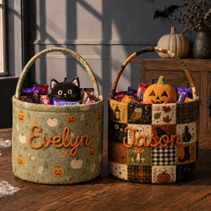 May include: Two cylindrical fabric baskets with handles, filled with sweets. The left basket is sage green with orange pumpkins and the name Evelyn in orange script. The right basket features a patchwork pattern of autumn motifs and the name Jason in orange.