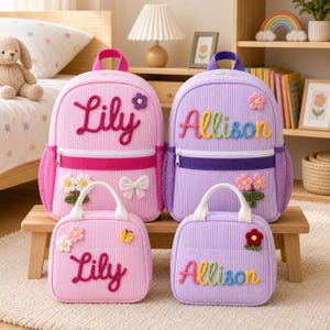 Könnte beinhalten: Zwei rosa und zwei lila Rucksäcke sowie Lunchtaschen aus Kord mit weißen Reißverschlüssen. Die Artikel sind mit den Namen Lily und Allison aus Garn bestickt und mit gehäkelten Blumen- und Schleifenapplikationen verziert.