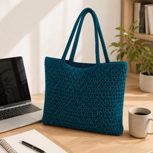Puede incluir: Un bolso tote rectangular de ganchillo en color azul cerceta profundo, con un patrón de punto abierto texturizado en todo el cuerpo y dos asas largas a juego. El bolso está hecho de hilo y mantiene una silueta estructurada con base plana.