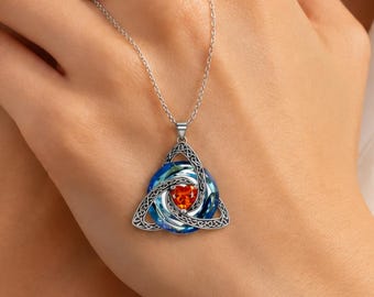 May include: A silver-toned necklace featuring a triangular pendant with intricate knotwork detailing. The center of the pendant contains a vibrant orange heart-shaped stone surrounded by swirling blue accents, suspended from a delicate silver chain.