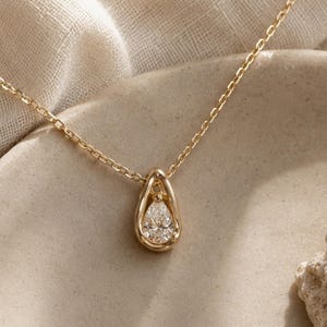 Puede incluir: Un collar de cadena dorada con un colgante en forma de lágrima. El colgante consiste en un marco dorado liso que rodea una única piedra preciosa transparente, tallada en forma de pera, situada en el centro. Incluye una fina cadena dorada.