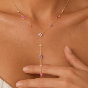 Könnte beinhalten: Eine goldene Y-Kette mit einer feinen Kette, die mit verschiedenen mehrfarbigen Edelsteinen in Rosa, Lila und klaren Tönen verziert ist. Die Steine sind in verschiedenen Formen wie oval, rechteckig und quadratisch gefasst und bilden einen Y-förmigen Anhänger.