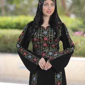 Puede incluir: Vestido negro con bordados florales en rojo, verde y azul. El vestido presenta mangas largas y un tocado a juego, mostrando patrones intrincados. El bordado se concentra en las mangas, el corpiño y el tocado.