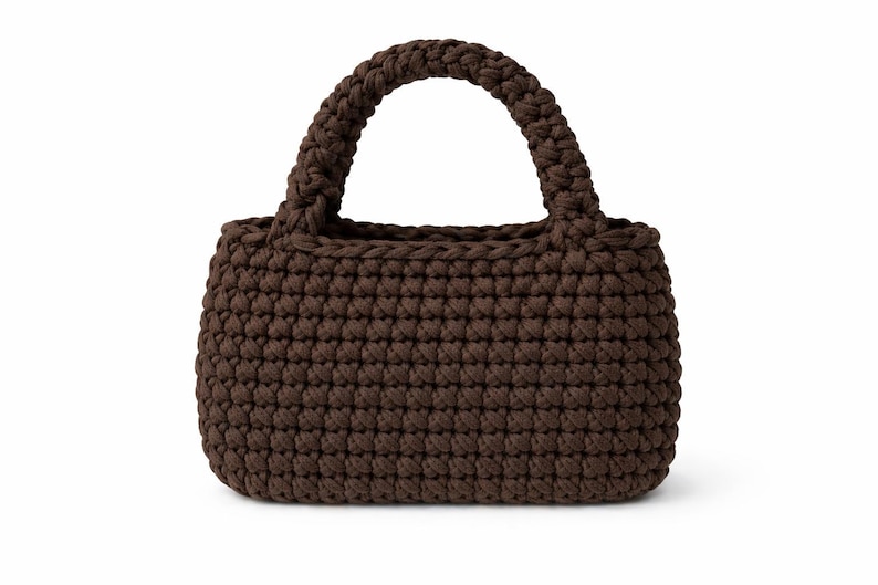 May include: A brown crochet handbag with a rectangular body and a rounded handle. The bag is made of a thick, textured yarn, and the handle is securely attached to the top of the bag. The bag is a solid color and appears to be handmade.