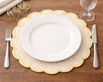 May include: A white ceramic plate sits atop a cream-colored, scalloped crochet placemat with a yellow border. A fork and knife are positioned on either side of the plate. A wine glass and a folded white napkin are also visible on the wooden table.