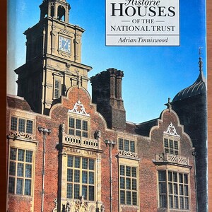 Può includere: Copertina di un libro raffigurante un edificio storico con un campanile e una facciata in mattoni. Il titolo è "Historic Houses of the National Trust" di Adrian Tinniswood, su uno sfondo di cielo blu.