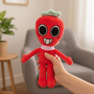 Könnte beinhalten: Ein rotes Plüschtier-Charakter mit großen schwarzen Augen, einem lächelnden Mund und einem kleinen rosa-weiß karierten Schal. Die Figur hat einen grünen Blätteraufsatz und rote Arme und Beine. Das Spielzeug wird in einer Hand gehalten.