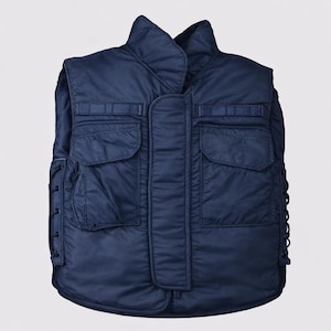May include: A navy blue sleeveless vest featuring a high collar, a central vertical placket, and two large front pockets with flaps. The sides of the vest are adjustable with black cord lacing, and the fabric has a smooth, quilted texture.