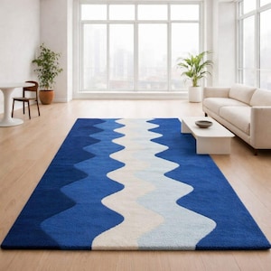 May include: A rectangular area rug with a wavy design in shades of blue and white. The rug is placed on a hardwood floor in a modern living room setting. The rug's dimensions are not visible.