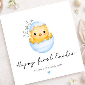 Op de afbeelding: Een witte Paas wenskaart met een aquarel illustratie van een geel kuiken dat uit een lichtblauw ei komt. De kaart leest "Happy first Easter" en "To an amazing son", met de naam "Charlie" boven het kuiken.