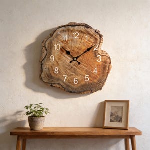 May include: A rustic wall clock crafted from a cross-section of a tree trunk. The clock features a natural wood grain pattern, white numerals, and black clock hands. The clock is mounted on a cream-colored wall. A small potted plant and framed picture sit on a wooden table below.