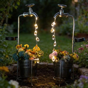 May include: Two solar-powered garden water features. Each has a faucet design with a stream of LED lights resembling water droplets. The faucets are mounted above metal buckets filled with colorful flowers, creating a decorative outdoor display.