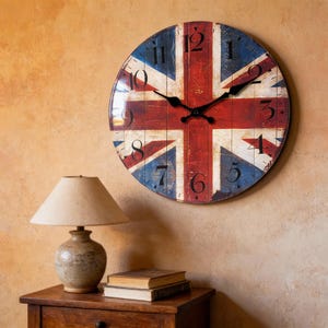 Può includere: Un orologio da parete rotondo con il design della bandiera Union Jack in rosso, bianco e blu. L'orologio ha lancette e numeri neri. L'orologio è montato su una parete marrone chiaro strutturata.