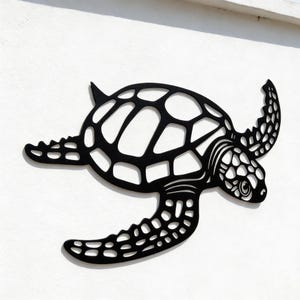 May include: A black metal sea turtle wall art piece. The turtle is depicted in a stylized, openwork design, with a detailed shell pattern and textured flippers. The artwork is mounted on a white wall, creating a high-contrast visual.