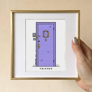 Peut inclure: Une impression encadrée carrée représentant une porte violette avec un cadre de judas jaune, une poignée jaune et un petit interphone sur le côté gauche. Le mot FRIENDS est imprimé en lettres capitales noires au bas de l'illustration.