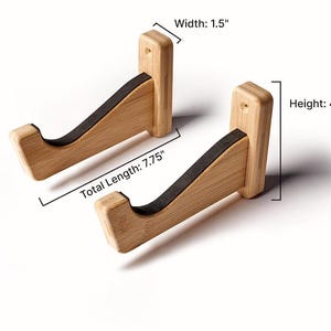 May include: Two light brown bamboo wall mounts with black padded cradles. Each mount features a width of 3.81 cm, a total length of 19.69 cm, and a height of 12.07 cm, with visible screw holes for mounting on a flat vertical surface.