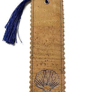 May include: A rectangular cork bookmark with a scalloped edge and a blue tassel. The bookmark features a stitched seashell design in blue and silver thread. A metal eyelet is at the top for the tassel.