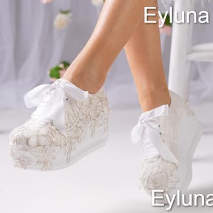 May include: White platform sneakers with intricate floral embroidery and pearl accents. The sneakers feature satin ribbon laces and are embellished with delicate beading. The image includes the text "Eyluna".