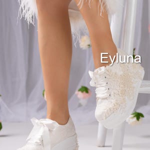 May include: White platform sneakers with lace and pearl embellishments. The sneakers have a ribbon lace-up closure and a bow detail. The brand name "Eyluna" is visible on the image.
