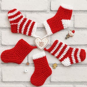 May include: A collection of five miniature, handmade Christmas stockings in red and white. Some stockings have white stripes, while others have white cuffs. A heart-shaped ornament and small decorative items are also present.
