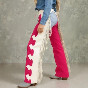 Puede incluir: Chaps de color rosa intenso con recortes decorativos blancos y flecos. Los chaps se combinan con una camisa vaquera y unos vaqueros azul claro. Tema western, usados con botas de vaquero grises.
