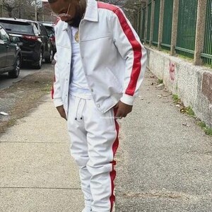 May include: A white tracksuit with red stripes on the sides. The jacket has a collared neckline and red stripes down the sleeves. The matching pants have a drawstring waist and are cuffed at the ankles. White sneakers complete the look.