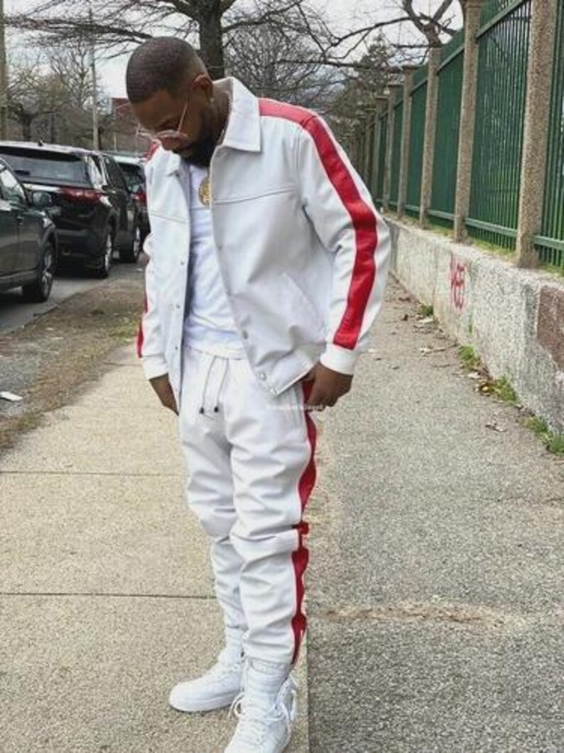 May include: A white tracksuit with red stripes on the sides. The jacket has a collared neckline and red stripes down the sleeves. The matching pants have a drawstring waist and are cuffed at the ankles. White sneakers complete the look.