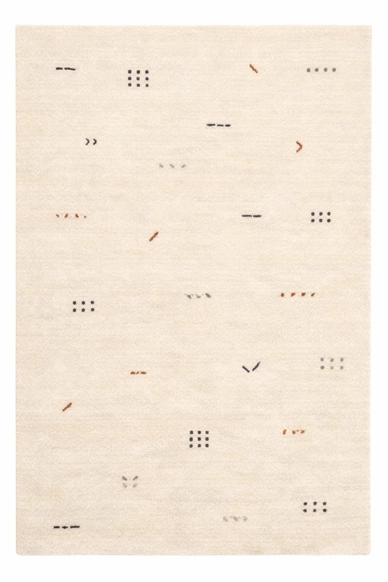 May include: Cream-colored area rug with a minimalist design. The rug features scattered geometric shapes in black, brown, and gray, including dashes, dots, and angled lines. The overall texture appears soft and inviting.