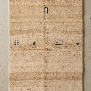 May include: Rectangular beige rug with a textured surface and a fringed edge. The rug features horizontal stripes and small black embroidered motifs, including a house and figures. A neutral-toned floor covering.