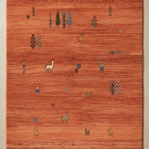 May include: An orange rectangular rug with a detailed pattern. The rug features stylized figures of trees, people, and animals in shades of green, yellow, and blue. The design is symmetrical, with a border of small geometric shapes.