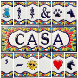 Könnte beinhalten: Eine Sammlung dekorativer Keramikfliesen mit verschiedenen Designs. Die Fliesen zeigen Bilder einer Katze, Toilettensymbole, ein kaufmännisches Und, einen Pfotenabdruck, einen Hund, das Wort "CASA", ein Komma, einen Bindestrich, eine Sonne mit Sonnenbrille, ein rotes Herz und ein Pferd.