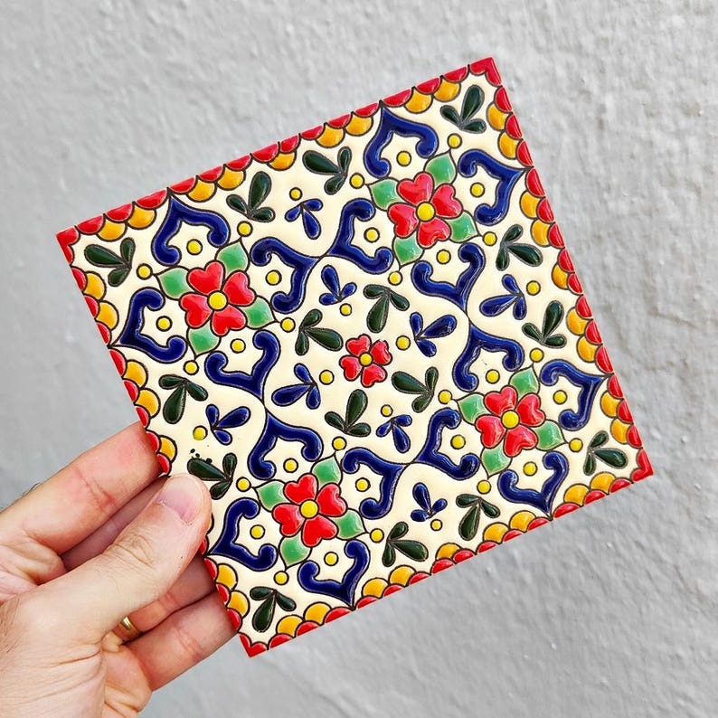 May include: Square ceramic tile with a vibrant floral pattern. The design features red, blue, yellow, and green elements on a cream background. The tile's edges are outlined in red, and the overall aesthetic is reminiscent of traditional decorative tiles.