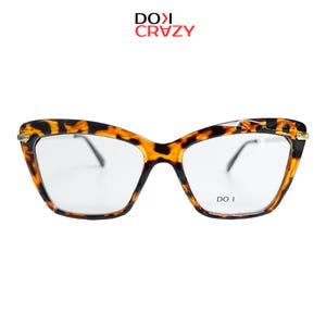 May include: Cat-eye spectacles with a tortoiseshell pattern. The frames are a mix of brown and black, with clear lenses. The brand name "DO I CRVZY" is printed at the top. The text "DO I" is printed on the lower right lens.