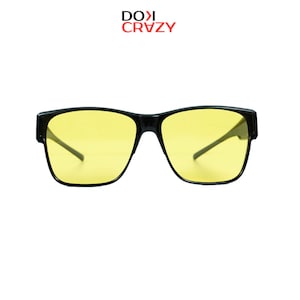 May include: Black-framed sunglasses with yellow lenses. The glasses have a rectangular shape and a sleek, modern design. The text "DOXI CRAZY" is in red above the glasses.