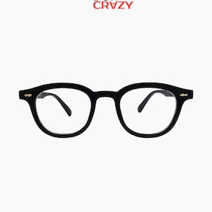 Puede incluir: Gafas negras de montura redonda con lentes transparentes. Las gafas tienen una montura gruesa y pequeños detalles dorados en las patillas. El texto "DOI CRZY" está en la esquina superior izquierda.