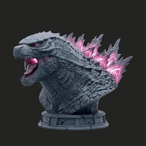 May include: A detailed bust of Godzilla in a grey colour scheme with pink accents. The sculpture features an open mouth, revealing a pink tongue and teeth. The dorsal fins are illuminated with pink light, and the bust sits on a decorative base.