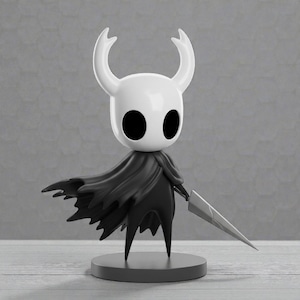 May include: A white and black figurine of a character with large horns, a cape, and a sword. The figure stands on a gray circular base. The character has large black eyes and a stylized design.