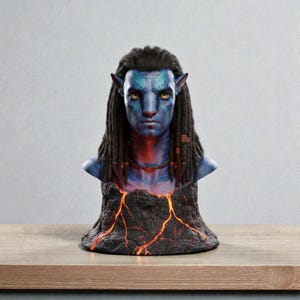 May include: A blue-skinned bust of a Na'vi character with yellow eyes and long black dreadlocks. The bust sits atop a base resembling volcanic rock with glowing orange cracks. The character has tribal markings.