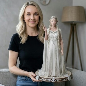 May include: A detailed figurine of a woman in a white gown with silver accents, standing on a decorative base. The figurine has long, flowing hair and is holding up one hand. The base is brown with silver embellishments. The figurine is approximately 12 inches tall.