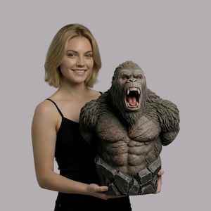 May include: A detailed bust of a gorilla with an open mouth, showcasing sharp teeth. The sculpture features a textured, gray fur and a muscular chest. It rests on a rocky base, creating a dynamic and powerful display.
