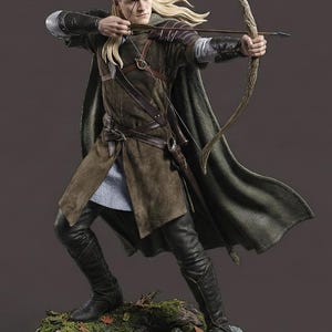May include: A detailed figurine of an archer in a forest setting. The archer is clad in a green and brown outfit, with a long cape and black boots. The figure is holding a bow and arrow, poised to shoot. The base is a detailed forest floor.
